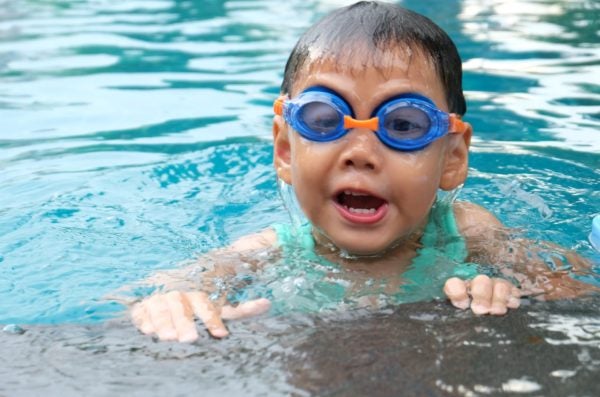 Child in the water holding onto edge of pool wearing goggles